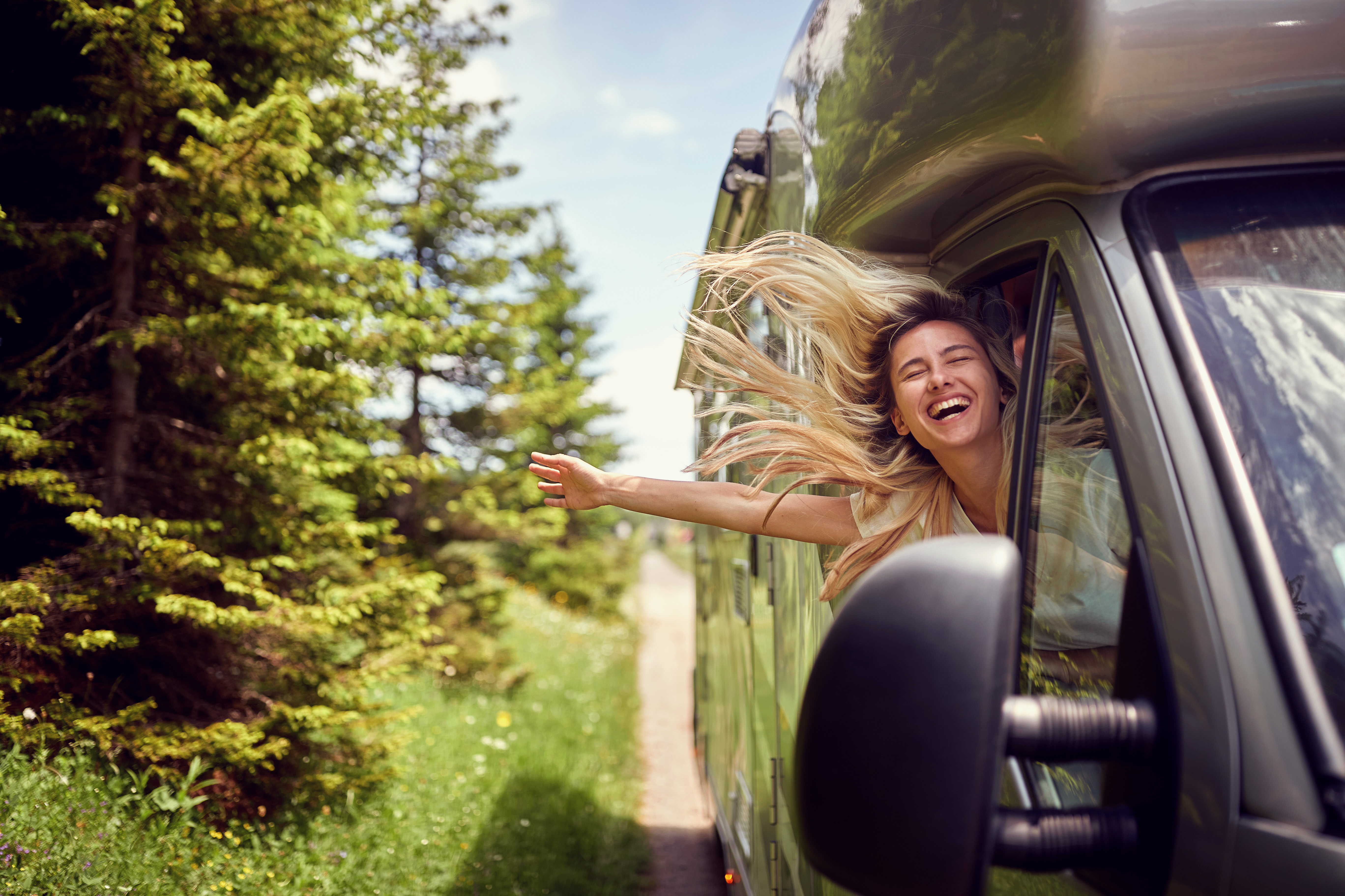 A woman with her hand out a motorhome driving down a forest road