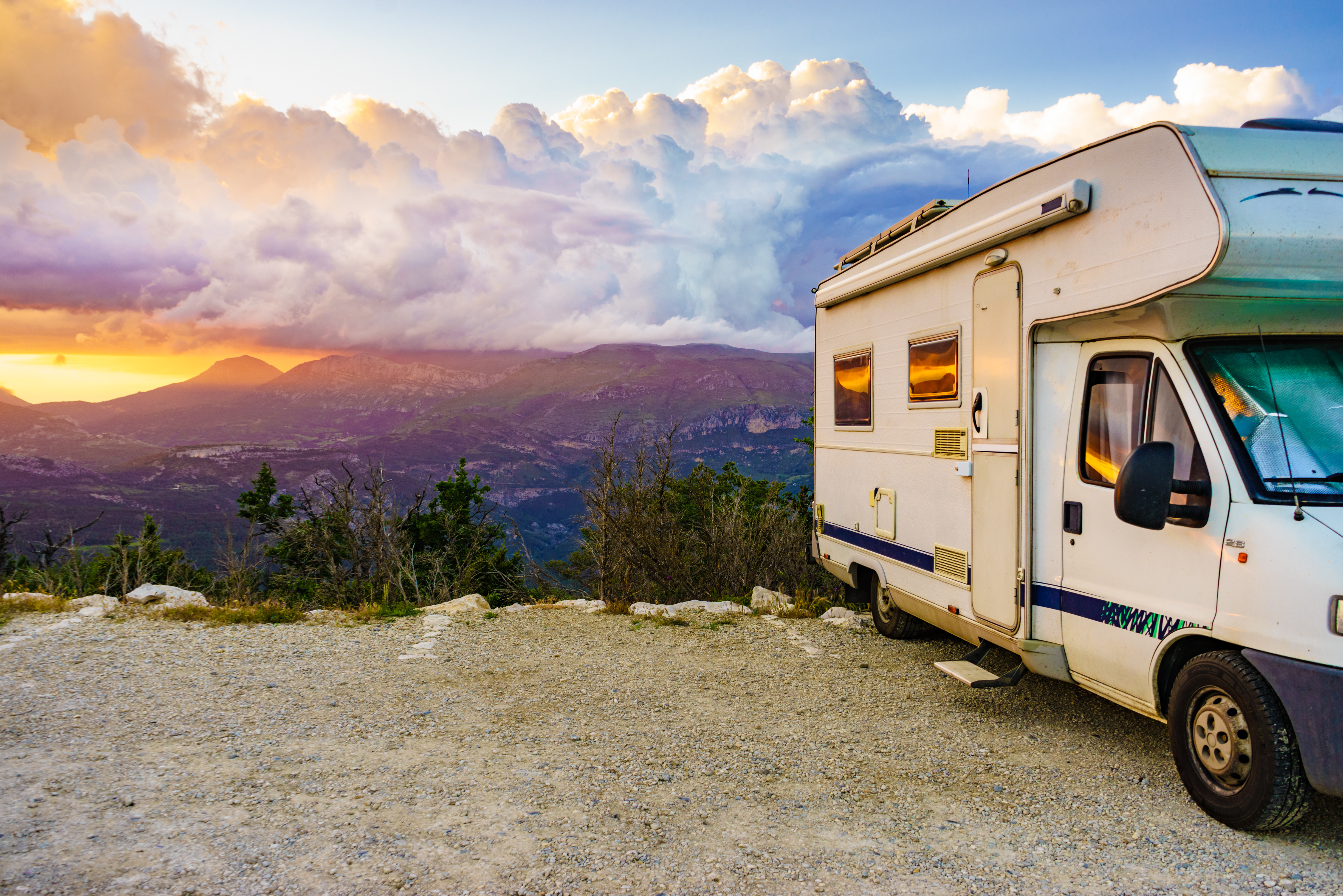 A motorhome near a cliff with mountains in the background at sunset