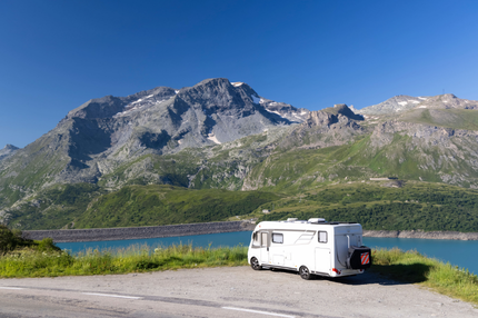 A motorhome parked near a lake with blue sky and mountains